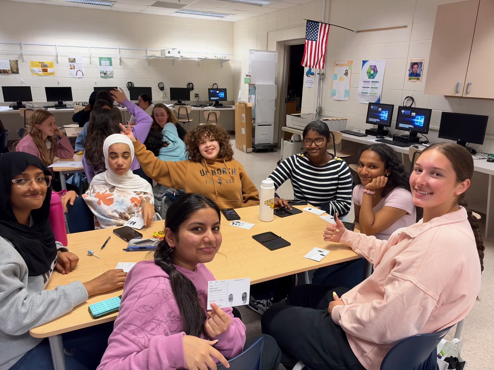 Students smiling around a table at a Girls in STEM workshop in a school computer lab